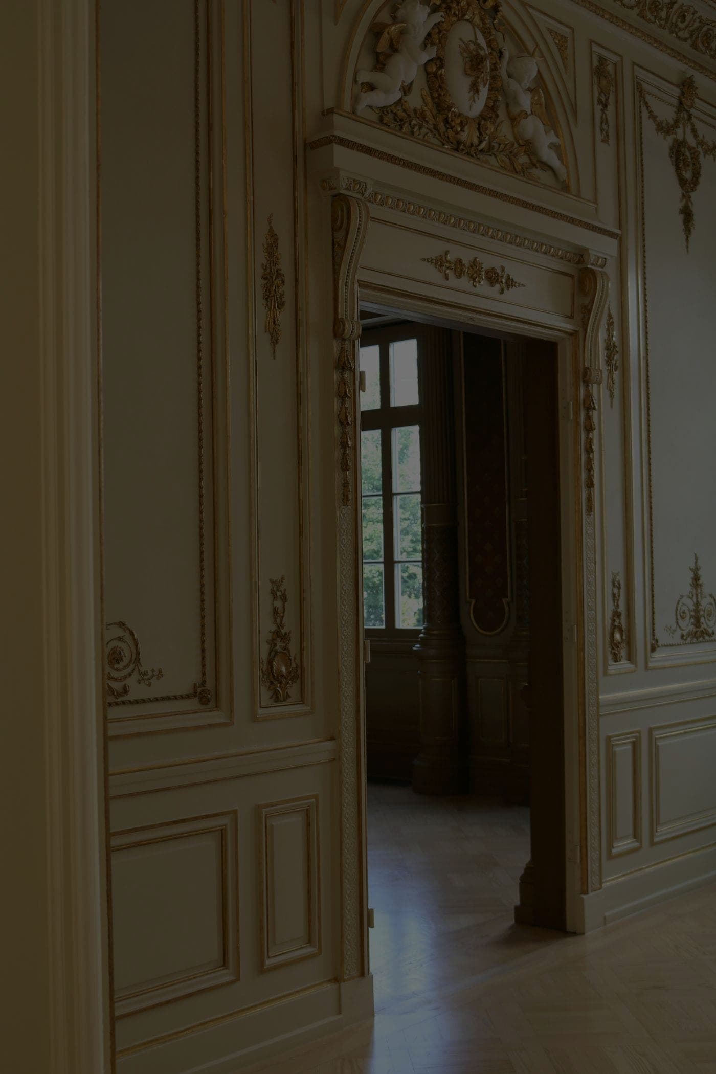 Enfilade d'un hôtel particulier : boiseries moulurées et dorées à la feuille, enfilade vers une porte-fenêtre, parquet à bâtons rompus