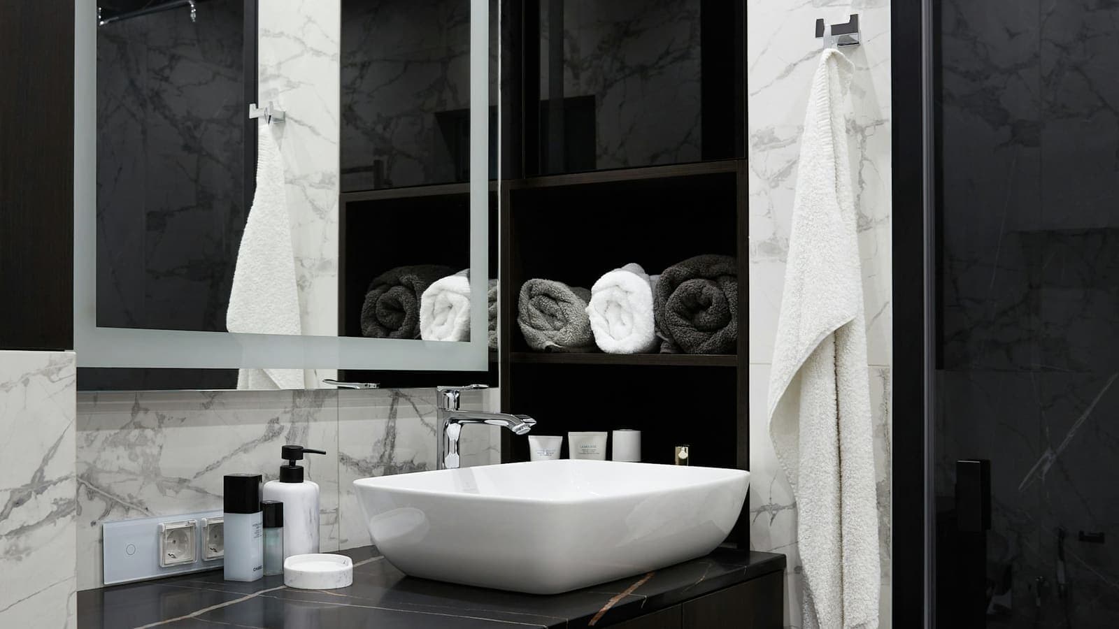 Salle de bain rénovée en marbre et bois sombre, vasque à poser sur un plan de toilette noir